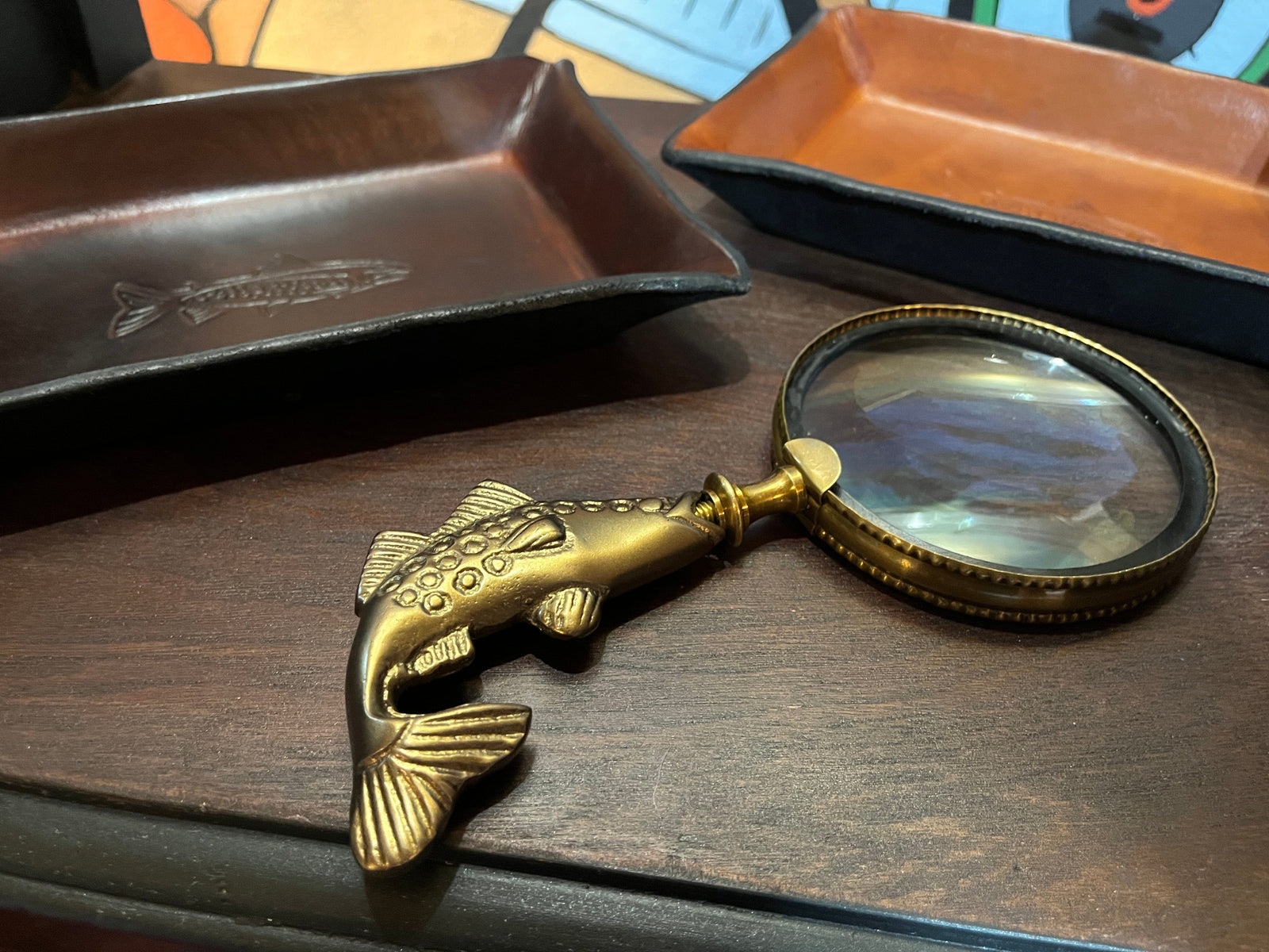 Brass fished shaped magnifying glass on a desk with leather trays in the background
