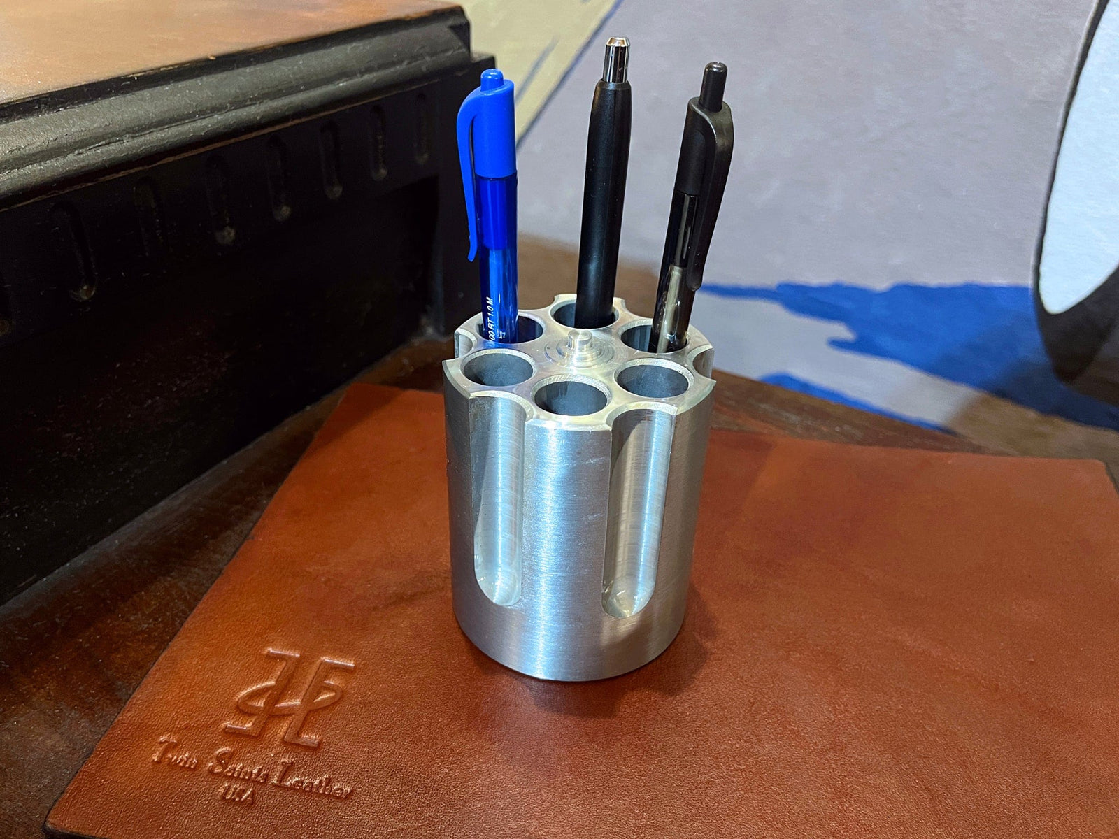Metal pen holder with three pens on a leather surface