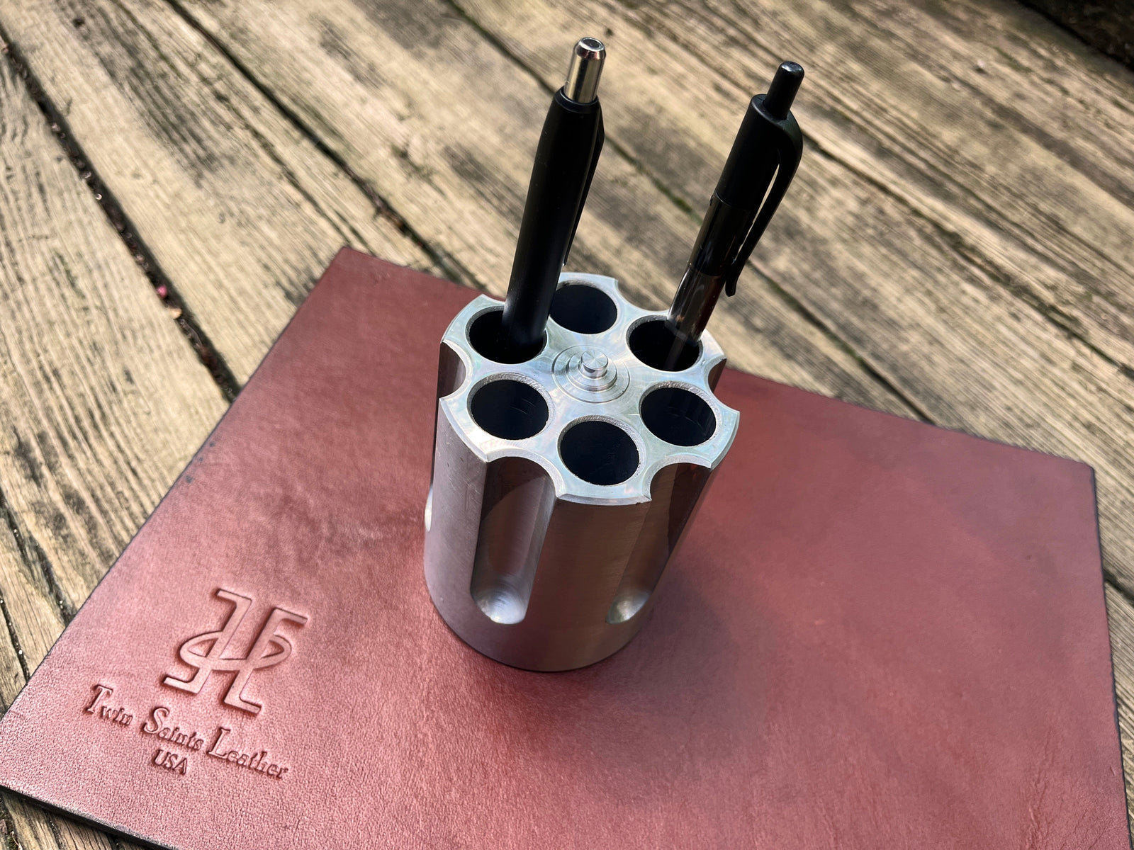 Pistol-shaped pen holder with three pens on a leather surface