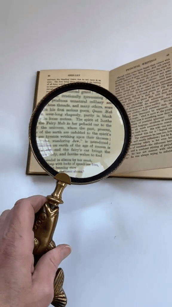 Hand holding a magnifying glass over an open book on a white surface