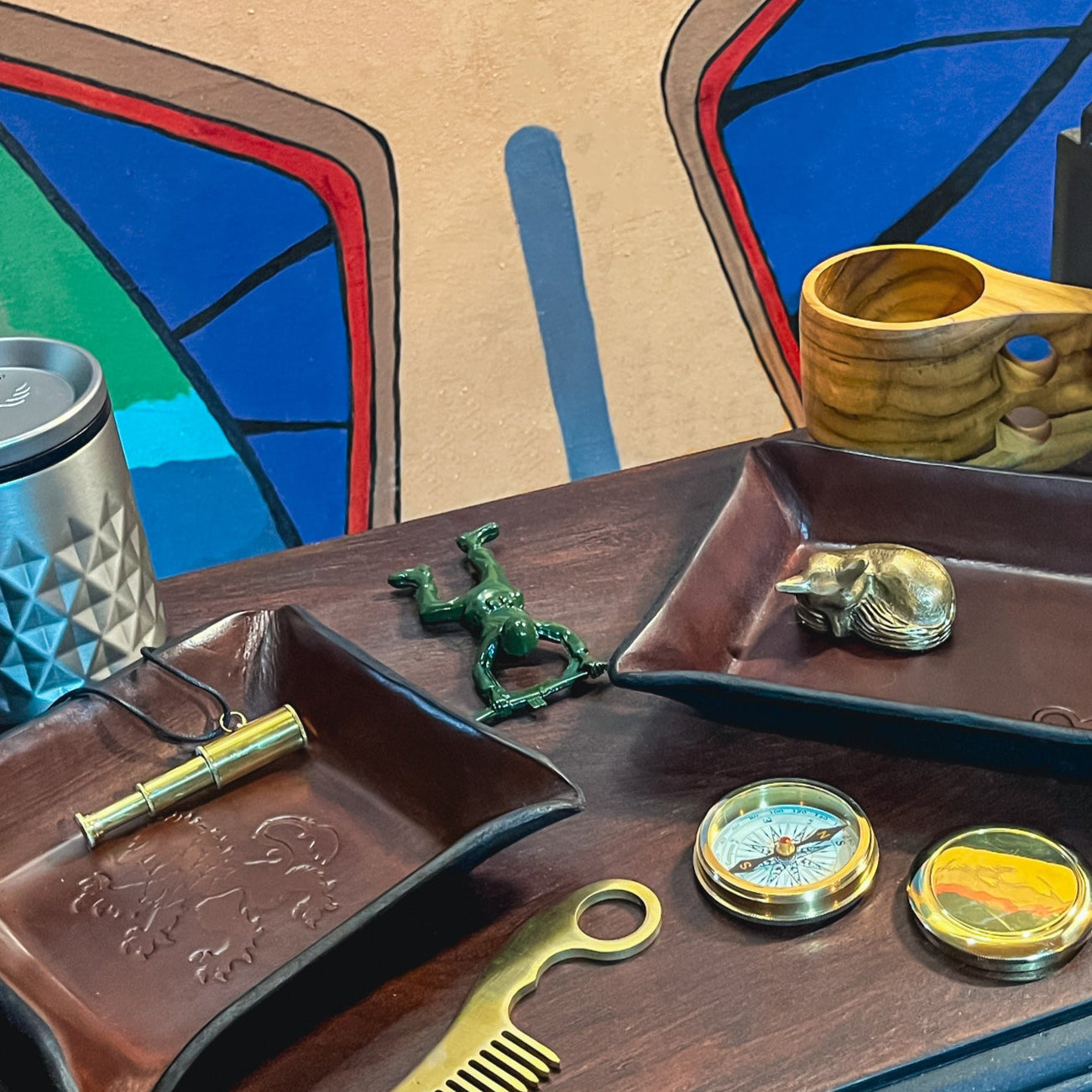 A collection of products for the modern adventurer shown on a desk with an colorful painting in the background