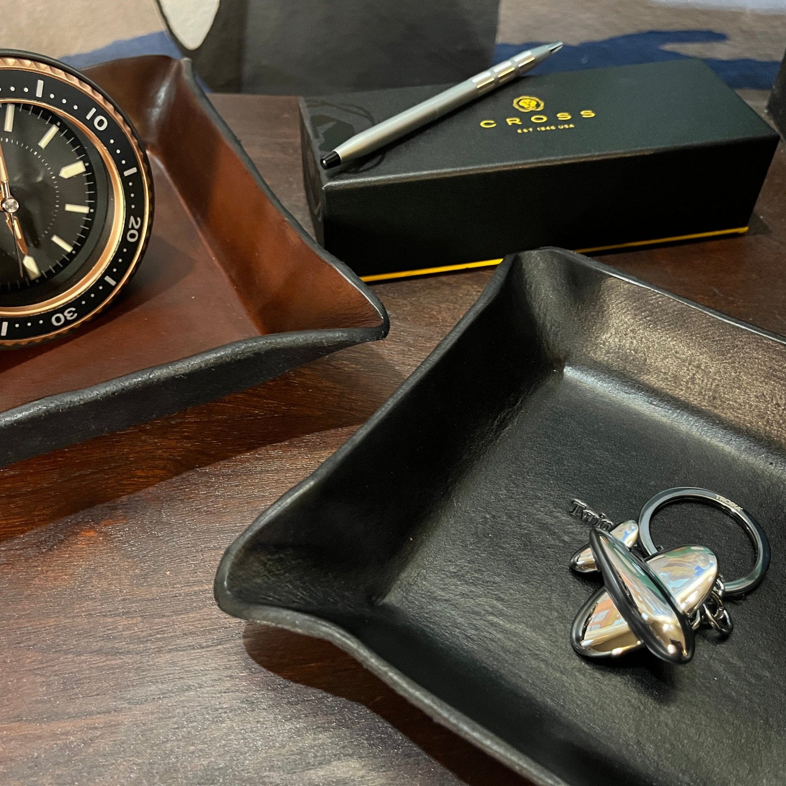 Leather valet trays, pen, and chrome keychain shown on a wooden desk