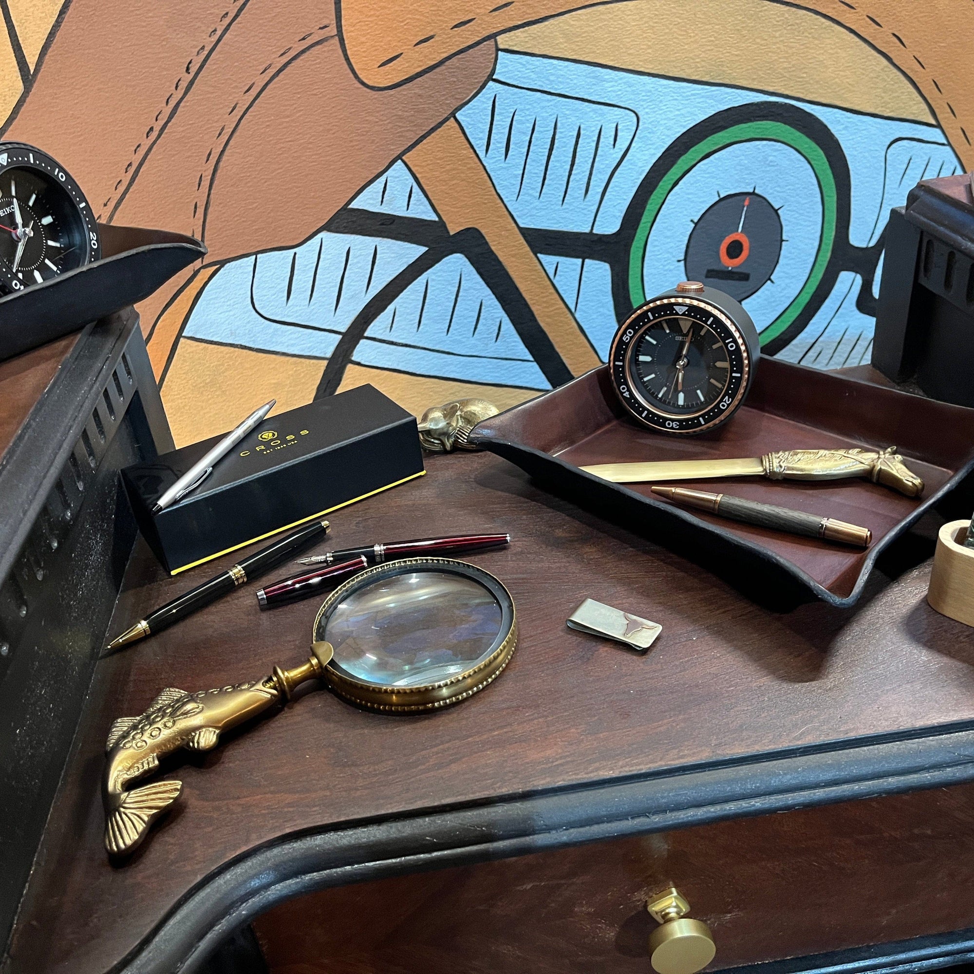 Vintage-style desk with pens, magnifying glass, and decorative items on a wooden surface.