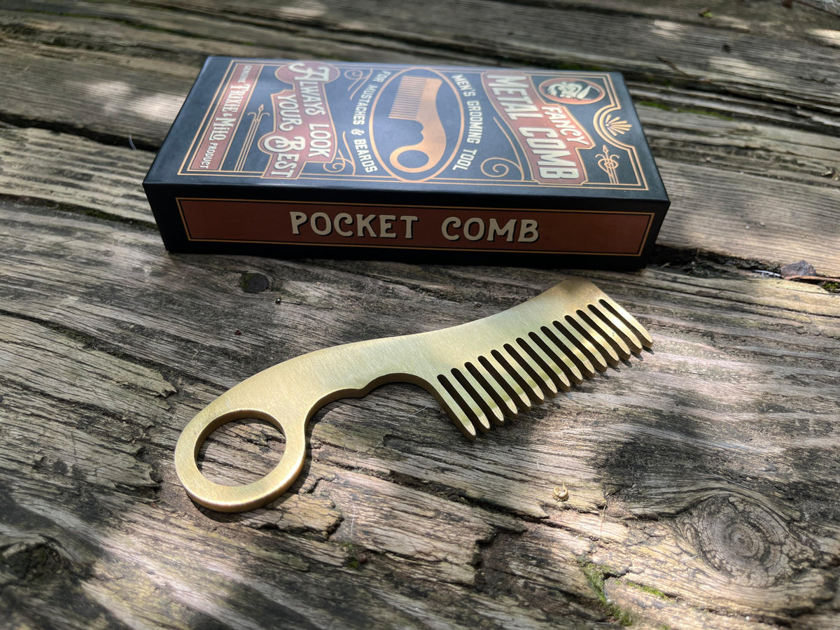 Brass colored metal grooming comb shown next to gift box