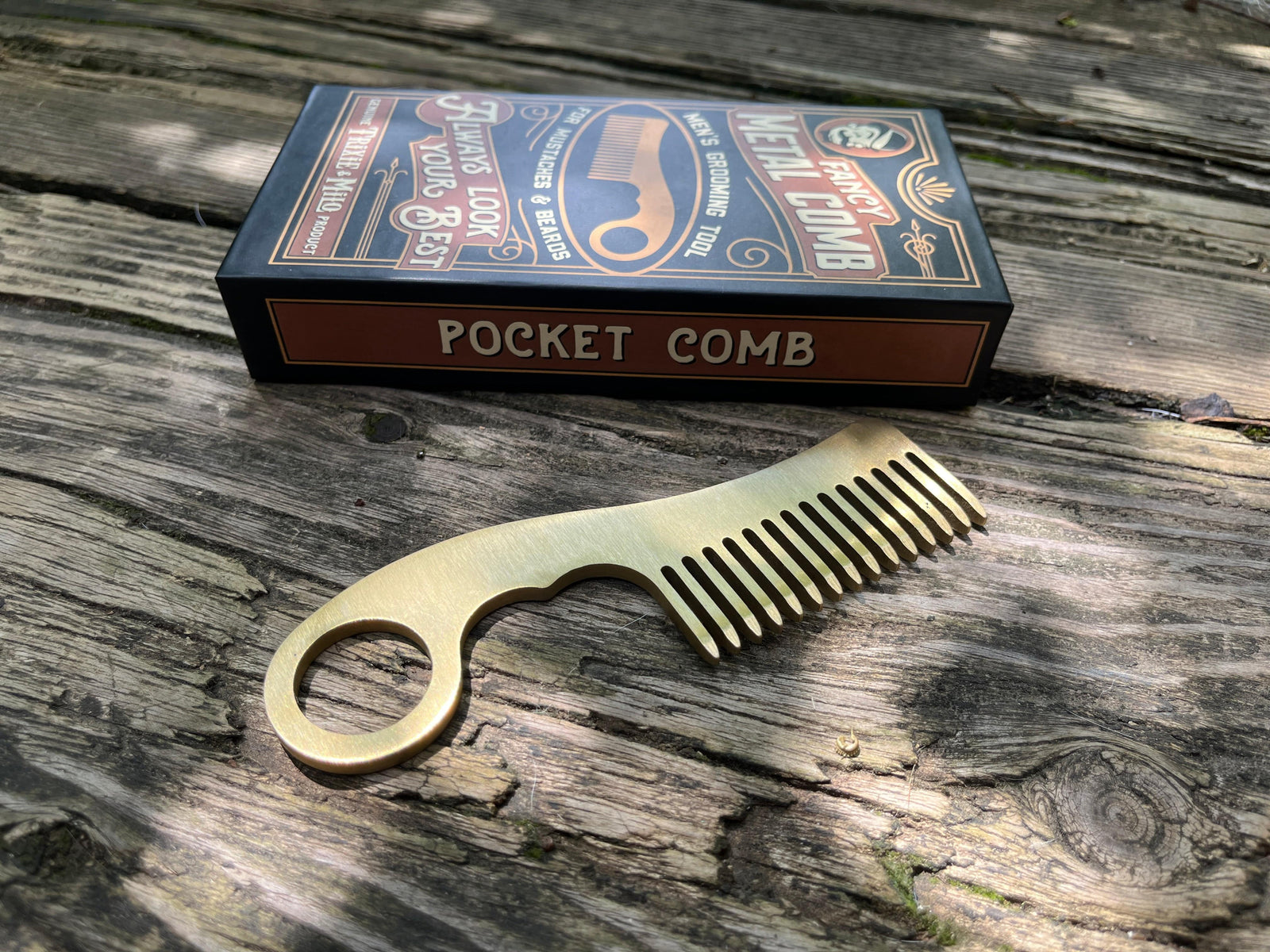 Brass colored metal grooming comb shown next to gift box