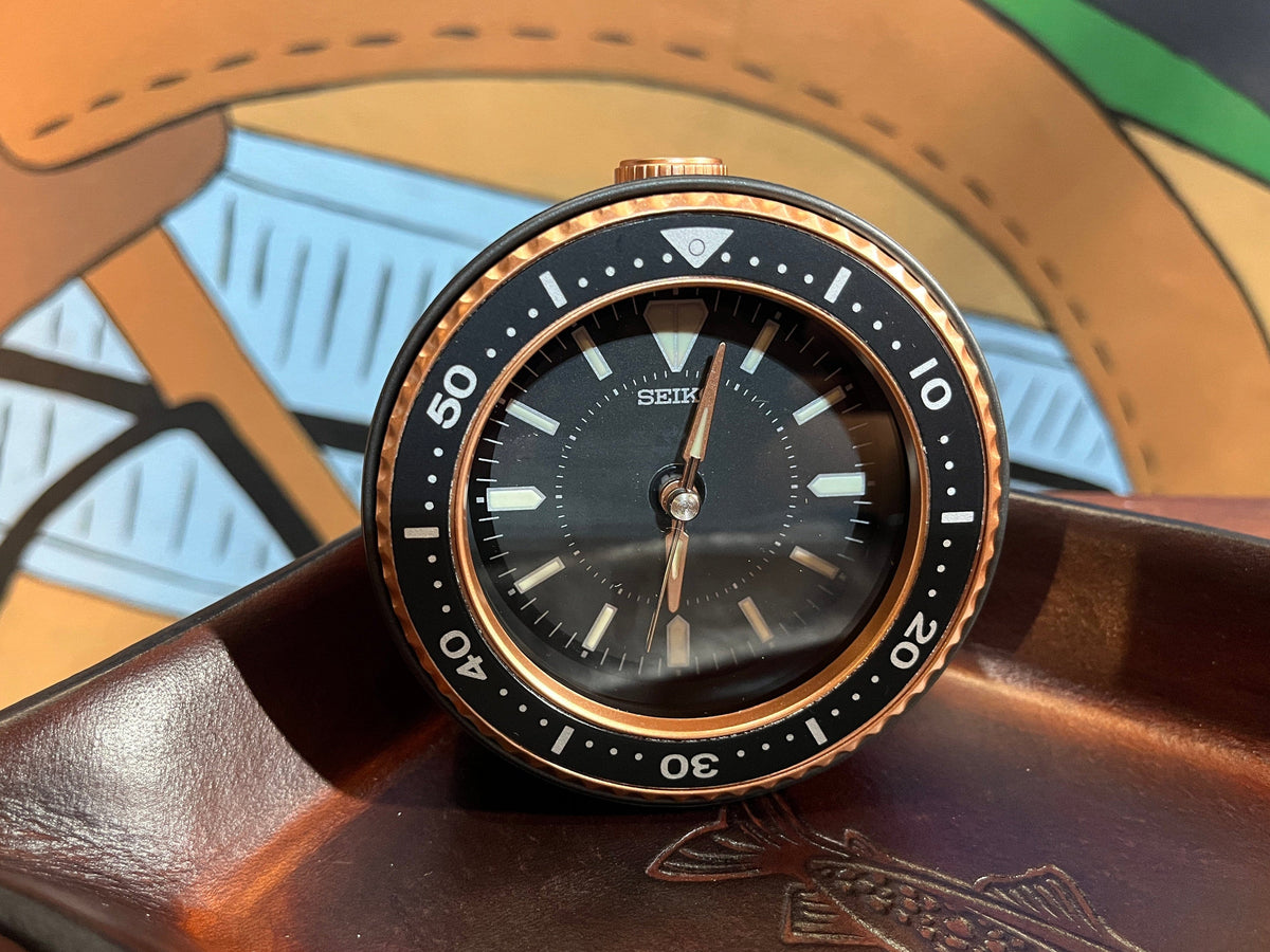 Seiko Mai dive style alarm clock in black and gold shown on desk