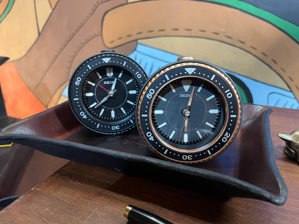 Seiko Mai alarm clocks shown on desk in black and metallic and black 