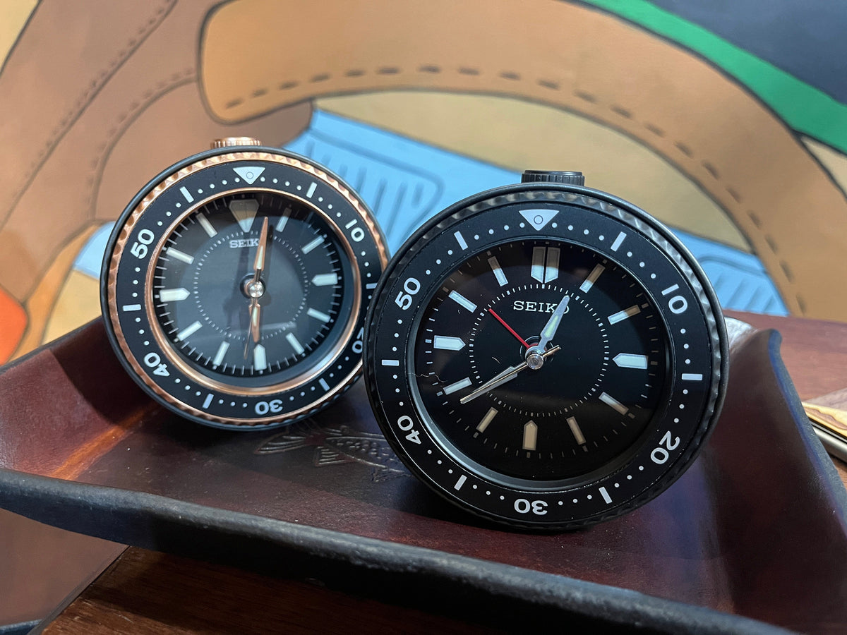 Seiko dive style alarm clocks with black/black shown in the front and black/metallic in the background