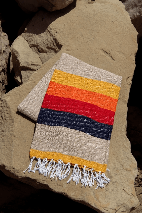 Tan, yellow, red, and navy recycled fiber blanket with fringe edge. Folded