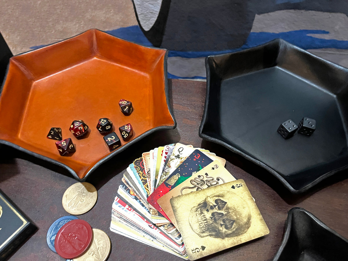 Two hexagonal dice trays, one brown and one black, with dice and playing cards on a table.