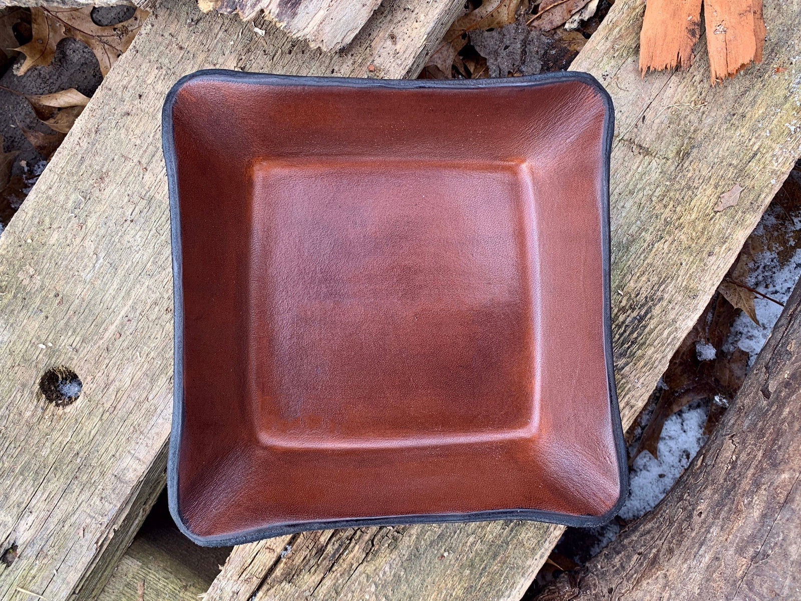 Square, brown leather valet tray shown on a wooden surface