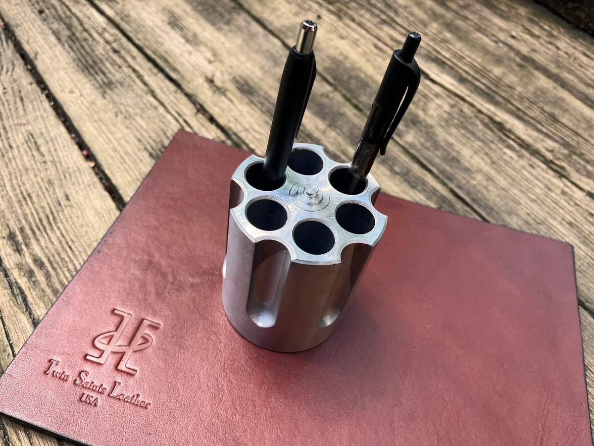 Pistol-shaped pen holder with three pens on a leather surface