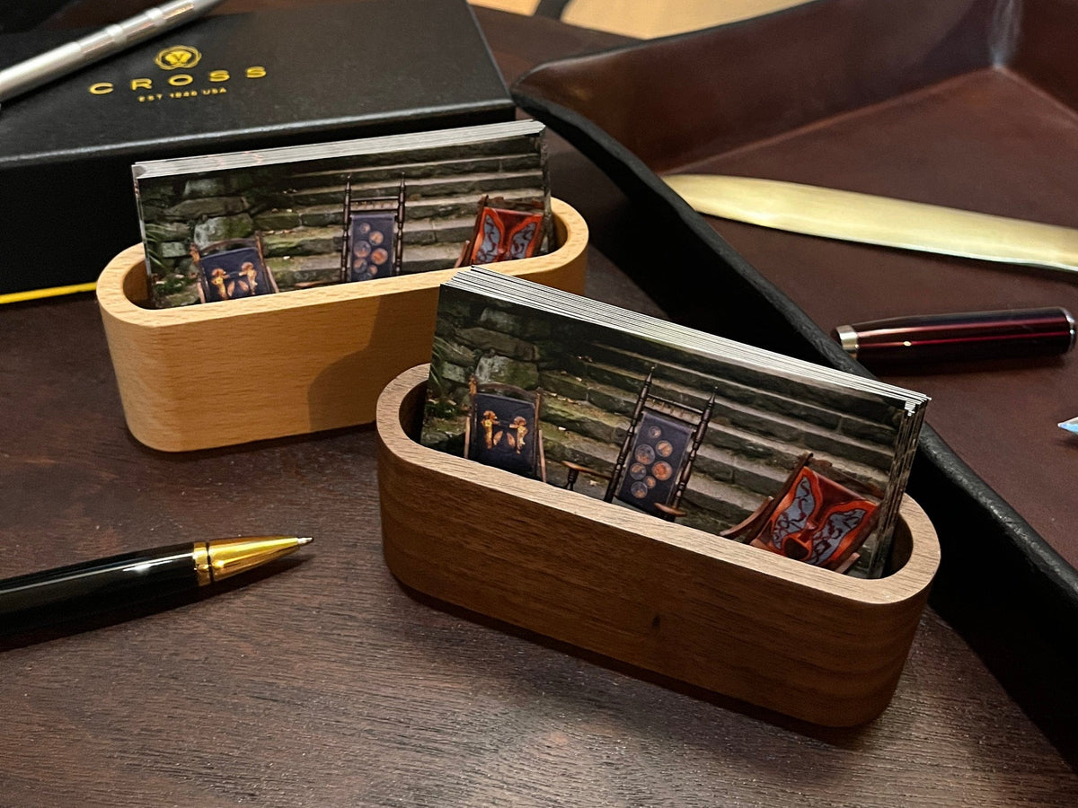 Wooden business card holder with business cards on a desk with a pen and Cross branded items.